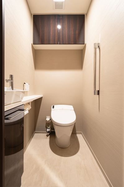 タンクレストイレ、手洗いカウンター、吊戸棚を備えた機能性の高いトイレ空間。